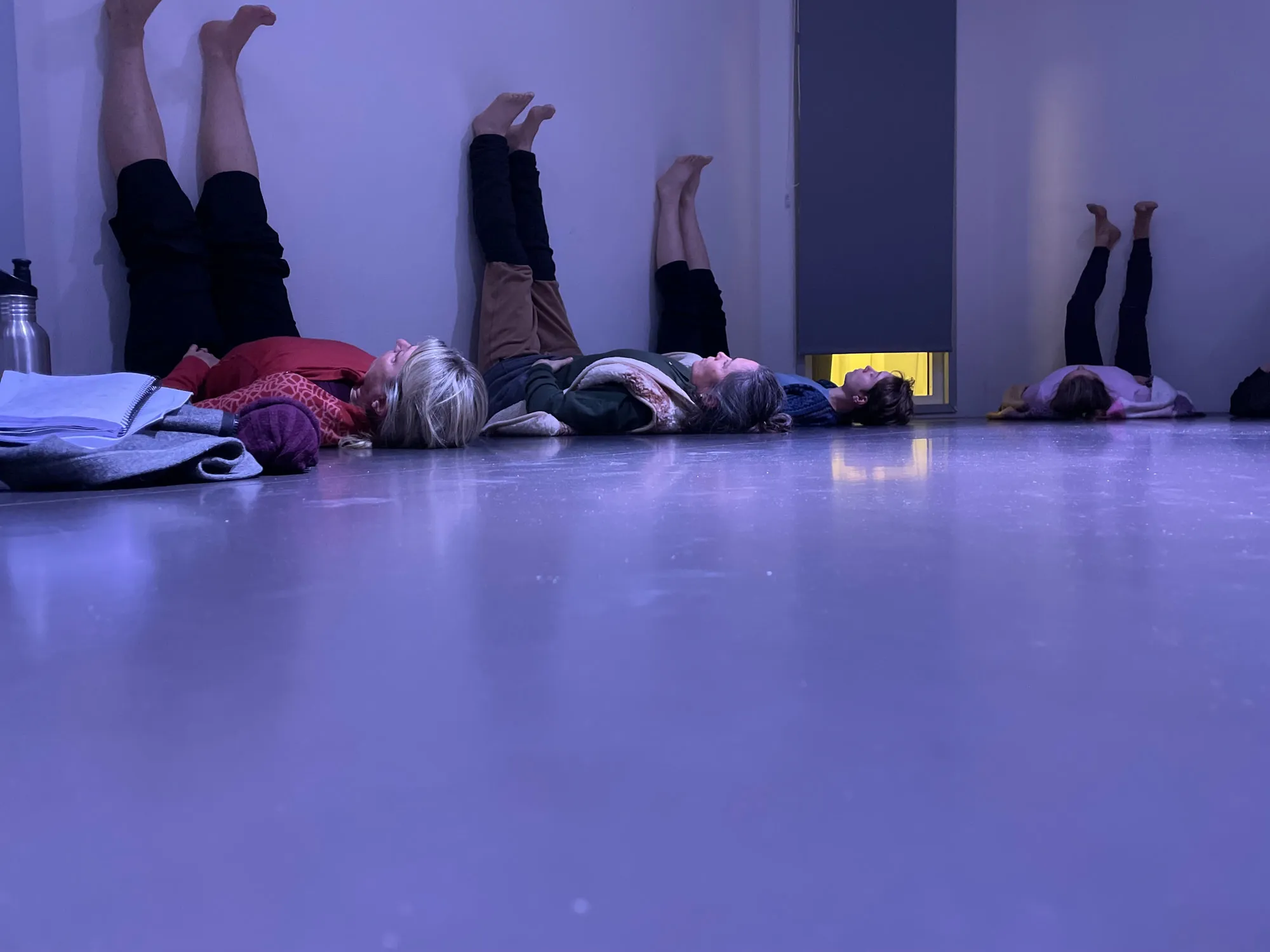 Deltagare ligger på ett studiogolv i violett ljus med benen upp mot väggen.